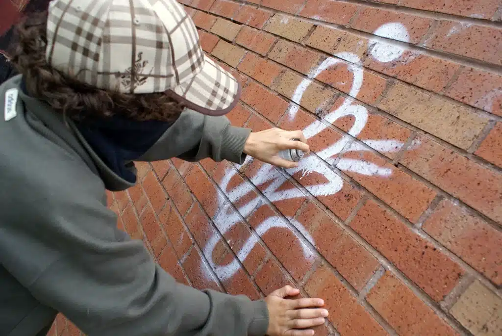 Youth spraying graffiti on a brick wall